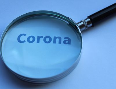 Foto zeigt eine Lupe über dem Schriftzug Corona