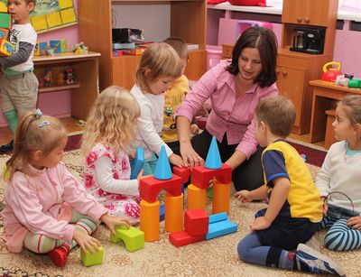Fünf Kindergarten im Kreis mit Erzieherin und Bausteinen