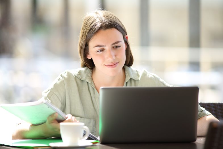 Eine junge Frau sitzt vor einem Laptop und liest.