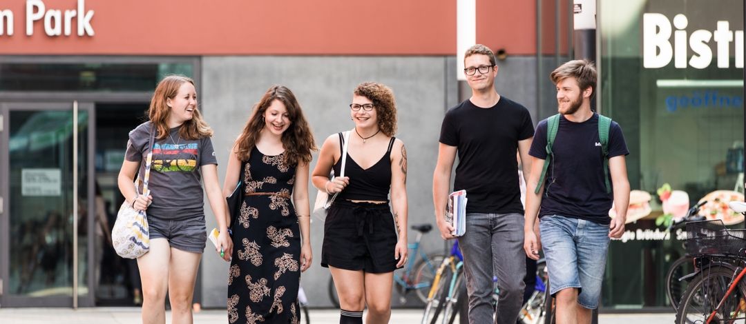 Studierende gehen nebeneinander auf dem Campusgelände