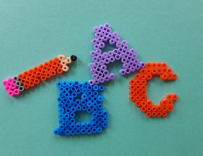 Darstellung von den Großbuchstaben A, B und C sowie eines Bleistiftes als Bügelperlenbild