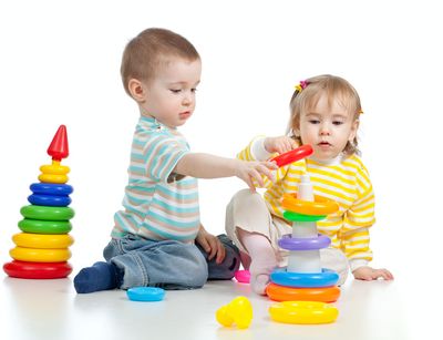 Zwei Kinder spielen auf dem Boden mit Spielzeug.