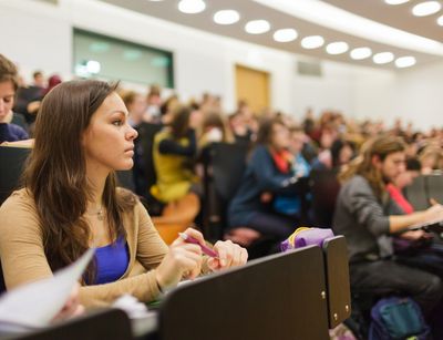 Fokus auf eine Studentin in der Vorlesung. Unscharf im Hintergrund sieht man den vollen Hörsaal, Foto: Christian Hüller 