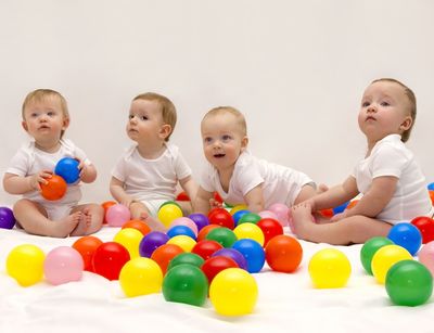 Vier Babies spielen auf dem Boden. Vor ihnen liegen bunte Plastikbälle.