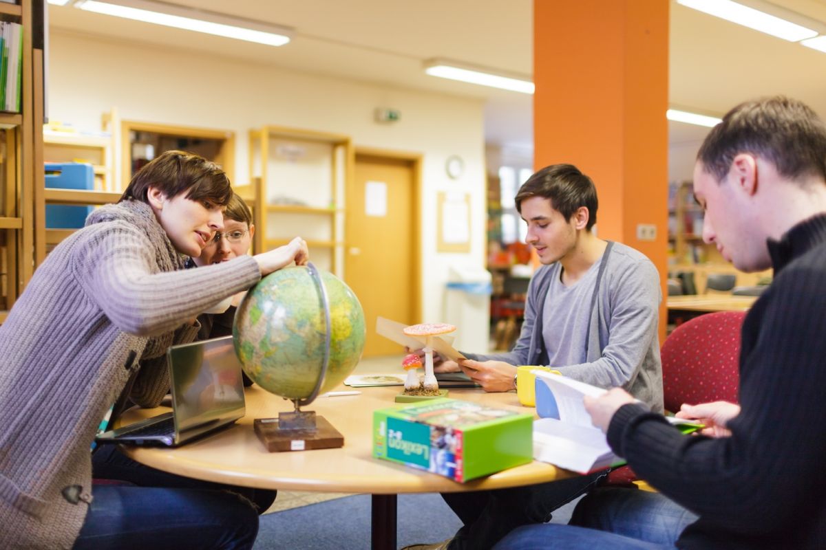zur Vergrößerungsansicht des Bildes: Foto: Drei Studierende der Erziehungswissenschaft in der Lernwerkstatt sitzen um einen runden Tisch herum und betrachten einen Globus