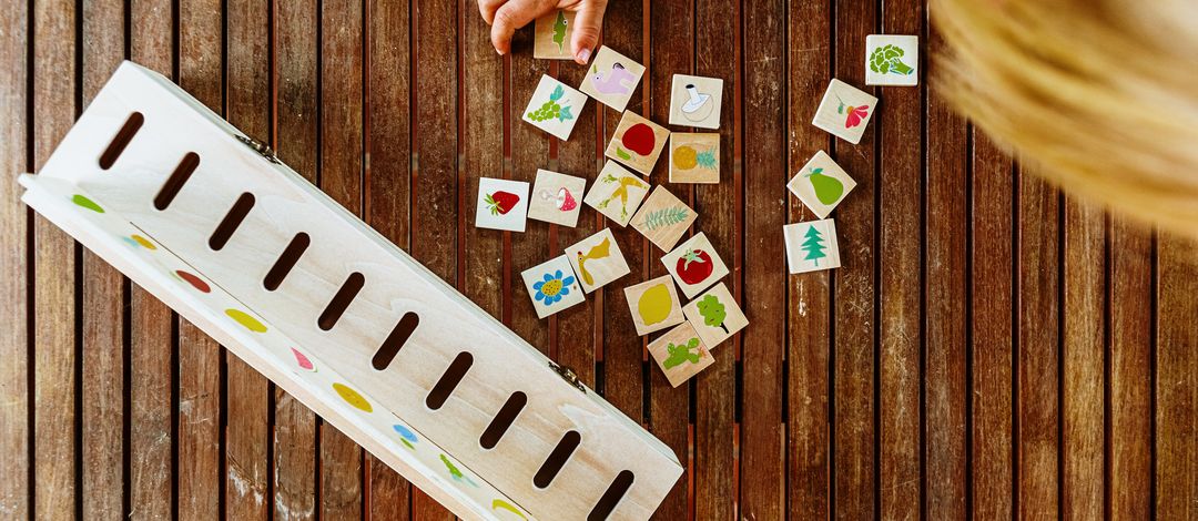 Ein Spiel für Kinder aus Holz, bestehend aus einer Box und quadratischen Spielsteinen, auf die bunte Bilder gedruckt sind.