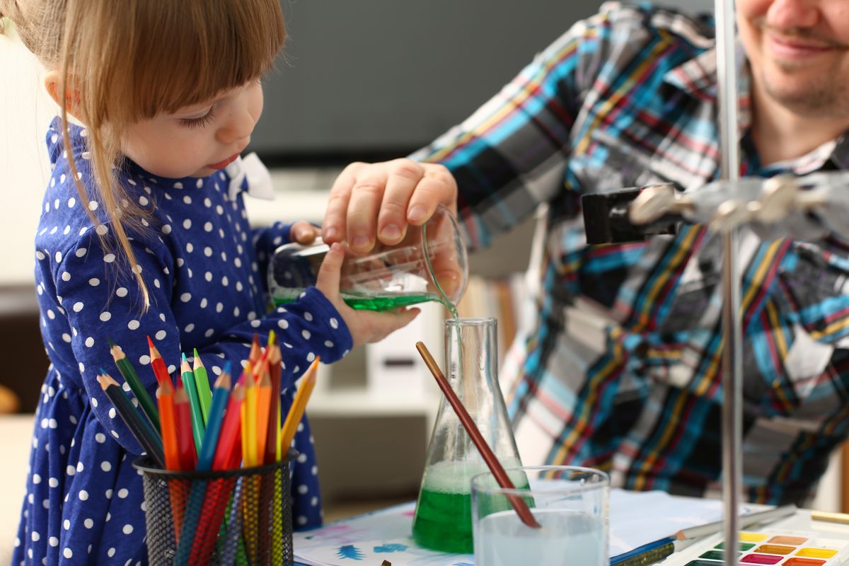 zur Vergrößerungsansicht des Bildes: Ein Kleinkind experimentiert mit seinem Vater mit Farben und gießt Flüssigkeit von einem ins andere Gefäß.