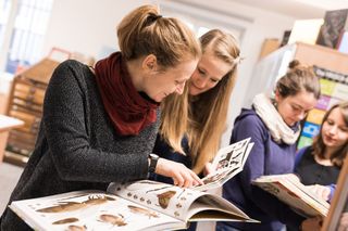 Jeweils zwei junge Frauen schauen sich im Vordergrund und im Hintergrund des Fotos ein Buch an.