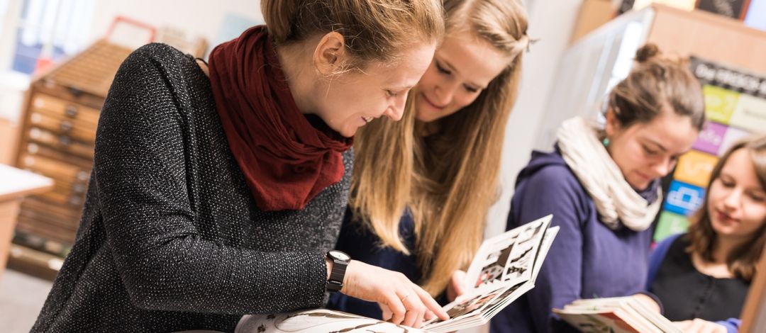 Jeweils zwei junge Frauen schauen sich im Vordergrund und im Hintergrund des Fotos ein Buch an.