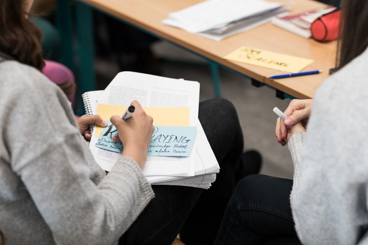 You can see two students sitting on chairs from behind. They are writing something on index cards