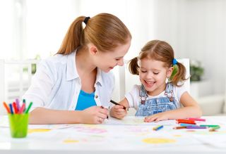 Junge Frau und ein Mädchen sitzen am Tisch und üben schreiben