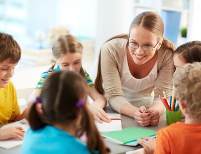 Lehrerin steht an einem Tisch, an dem fünf Schüler:innen arbeiten.