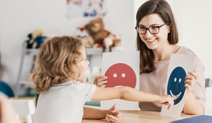 Frau zeigt Kind Karten mit abgebildeten Emotionen