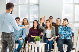 mehrere in Stuhlreihen sitzende Personen mit einem Referenten im Vordergrund