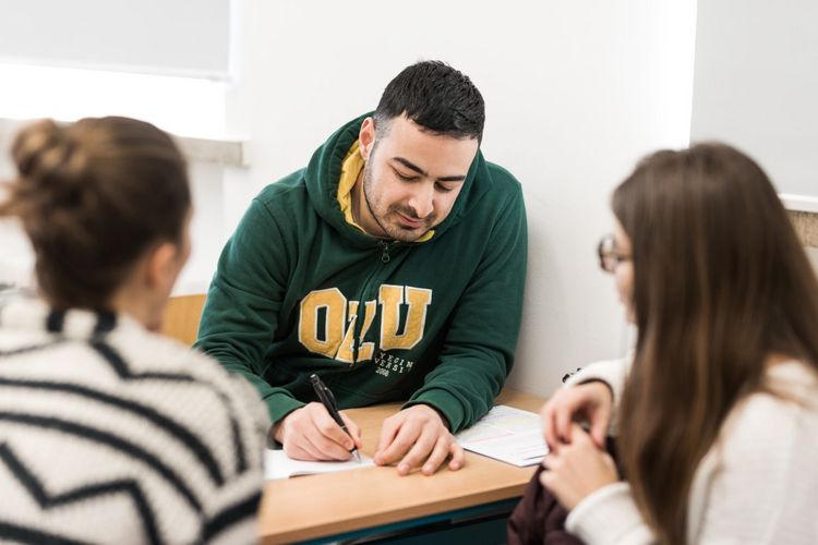 A male and two female students sit opposite each other at a table and work on tasks together