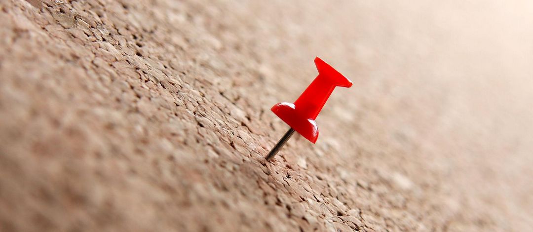 Close-up of a red pin stuck on a pinboard.