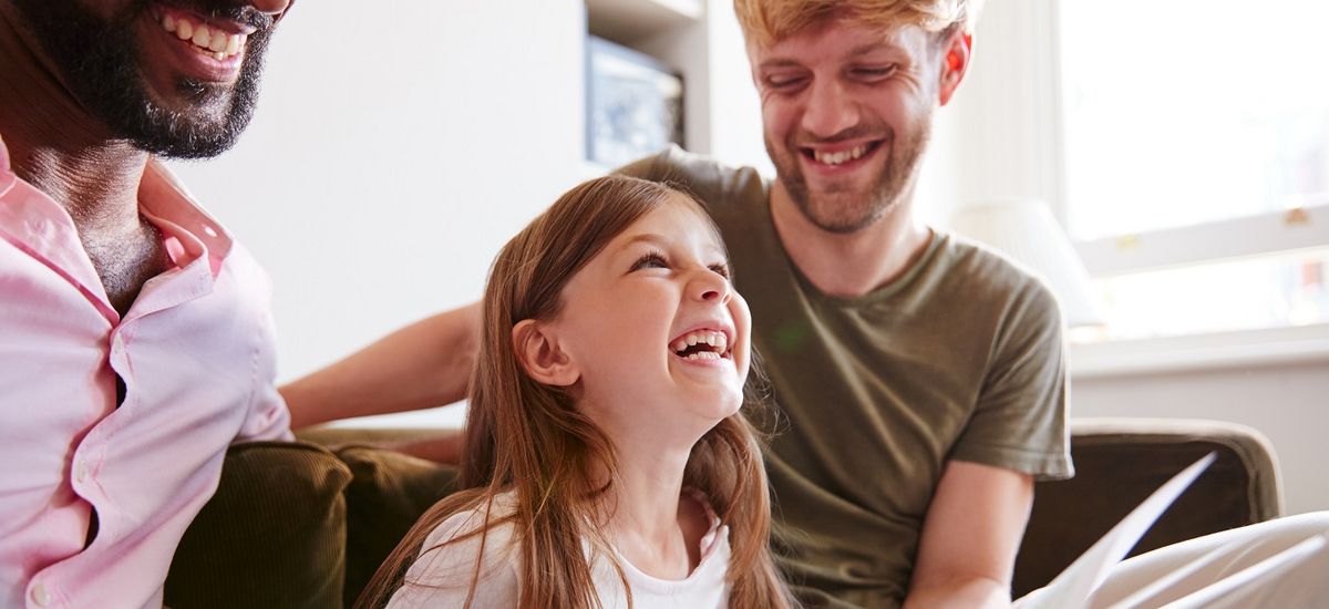 2 Erwachsene betrachten gemeinsam mit Kind ein Buch und lachen