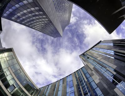 Blick vom Campus Augustusplatz in den Himmel. Das futuristiche Augusteum, der Uniriese und das Gebäude der Mensa reihen sich kreisförmig um den blauen Ausschnitt des Himmels herum.