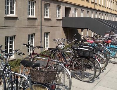 Farbfotografie eines Hauseinganges, vor dem Haus stehen Fahhradständer.