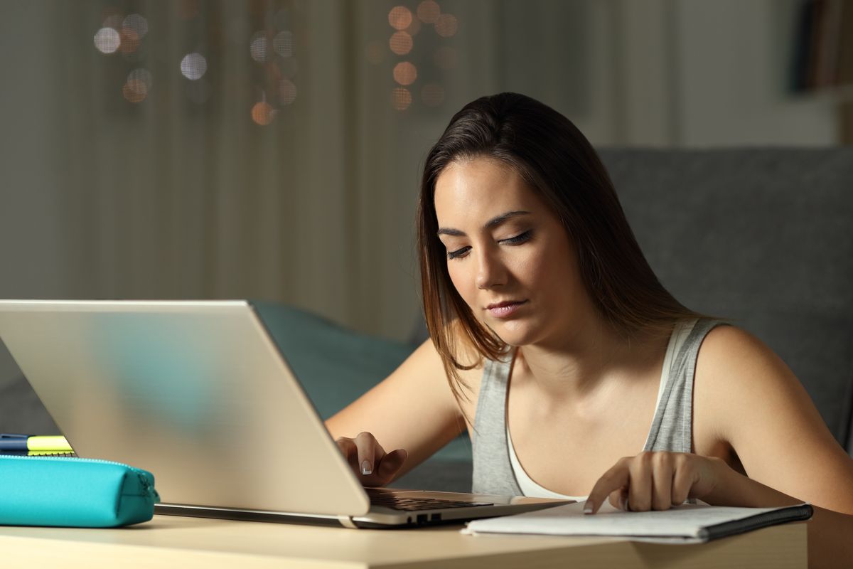 Eine junge Frau sitzt vor einem Laptop und liest
