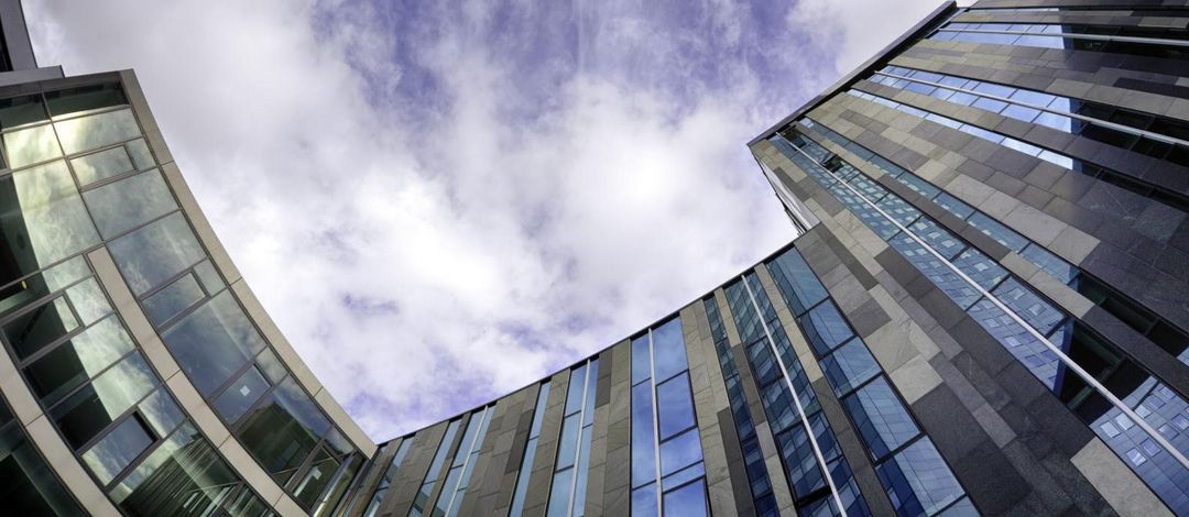 Blick vom Campus Augustusplatz in den Himmel. Das futuristiche Augusteum, der Uniriese und das Gebäude der Mensa reihen sich kreisförmig um den blauen Ausschnitt des Himmels herum.