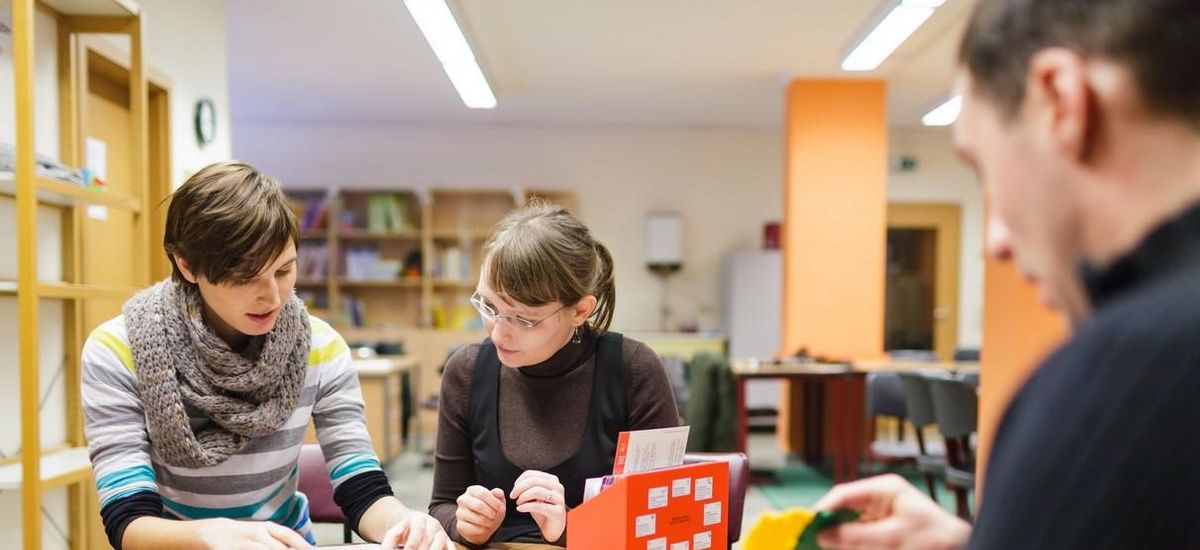 Drei Studierende sitzen zusammen an einem Tisch auf dem Arbeitsblätter und mathematische Modelle stehen, Foto: Christian Hüller