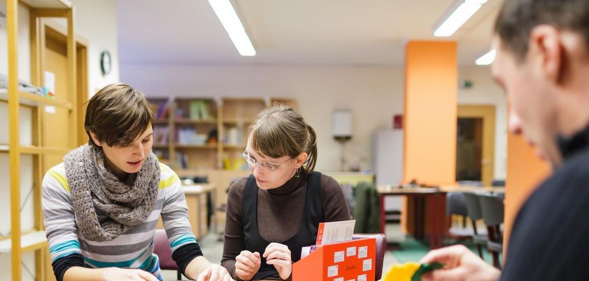 Drei Studierende sitzen zusammen an einem Tisch auf dem Arbeitsblätter und mathematische Modelle stehen, Foto: Christian Hüller