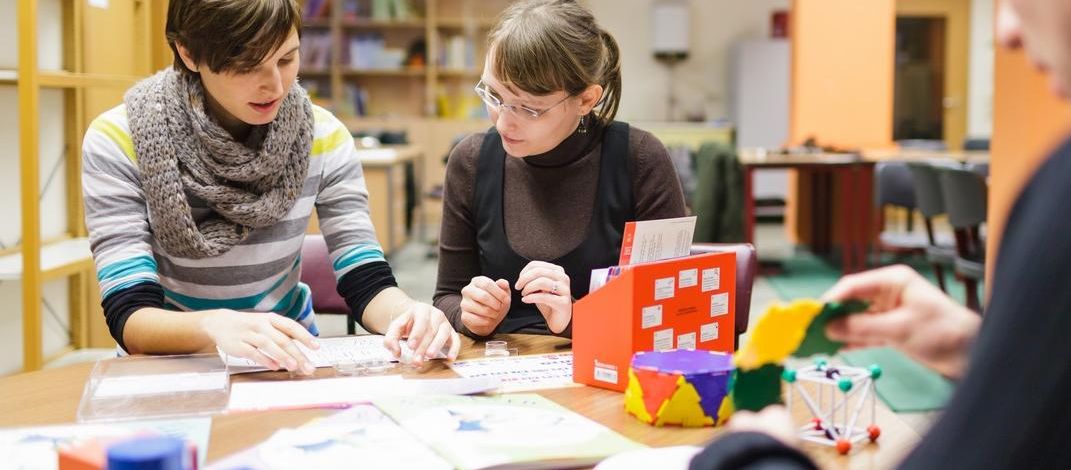 Drei Studierende sitzen zusammen an einem Tisch auf dem Arbeitsblätter und mathematische Modelle stehen, Foto: Christian Hüller