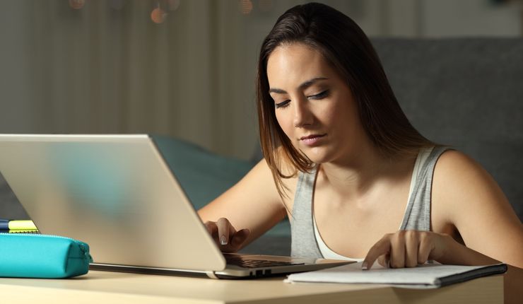 Eine junge Frau sitzt vor einem Laptop und liest